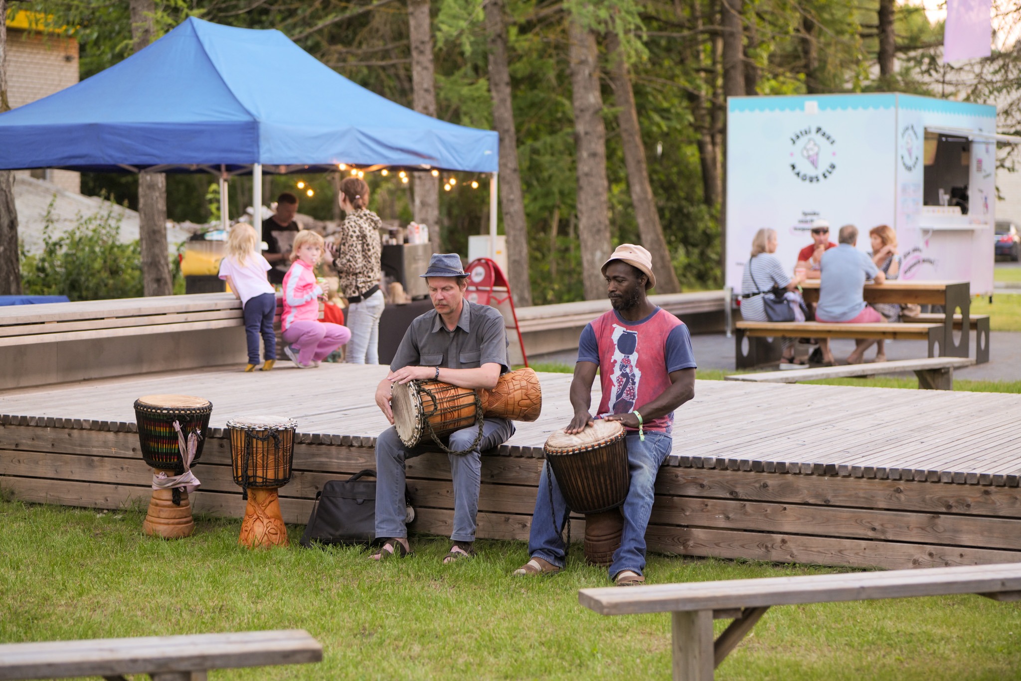 Two musicians play djembe on the outdoor stage, in the evening