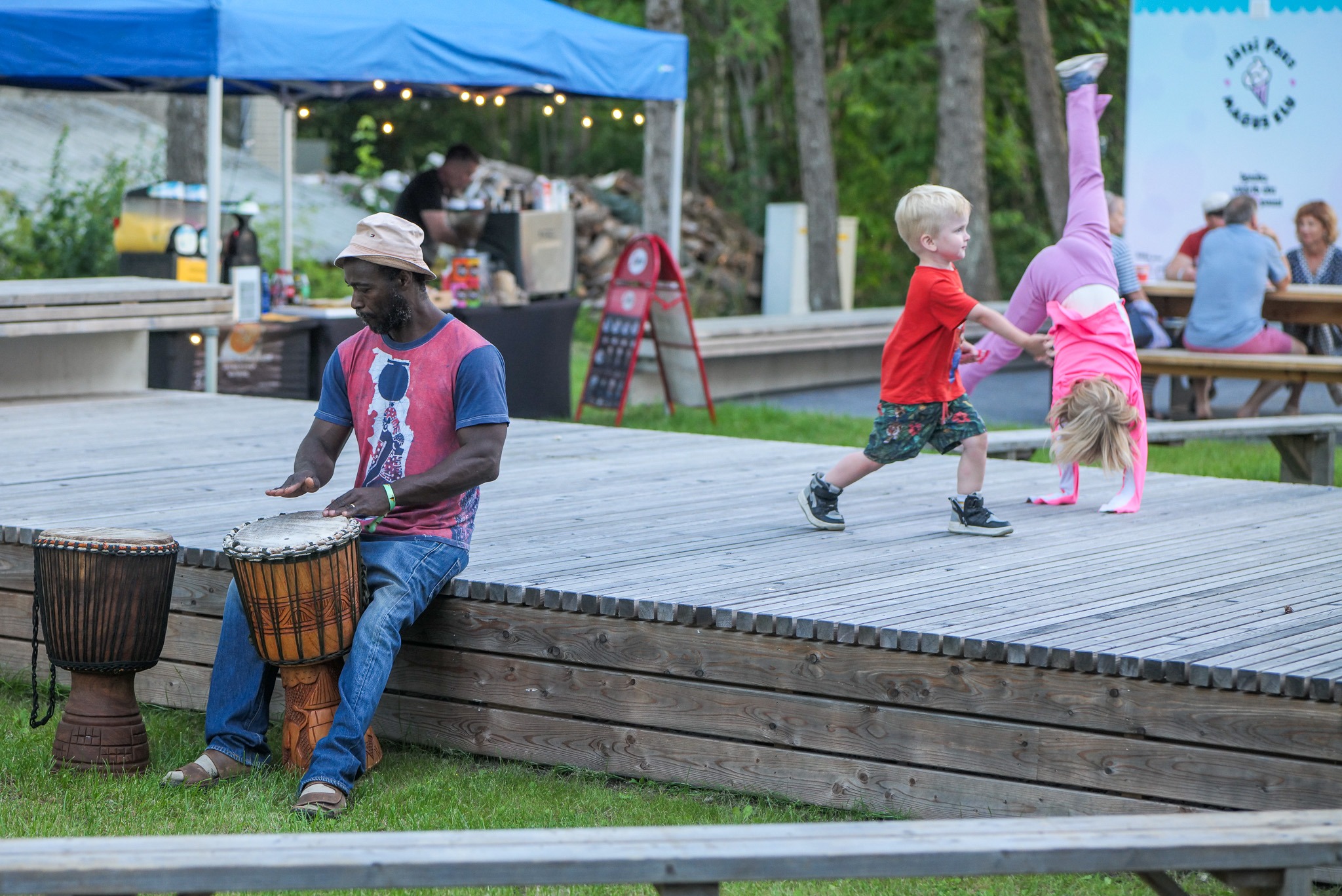 The seller plays djembe alone on stage while children play nearby