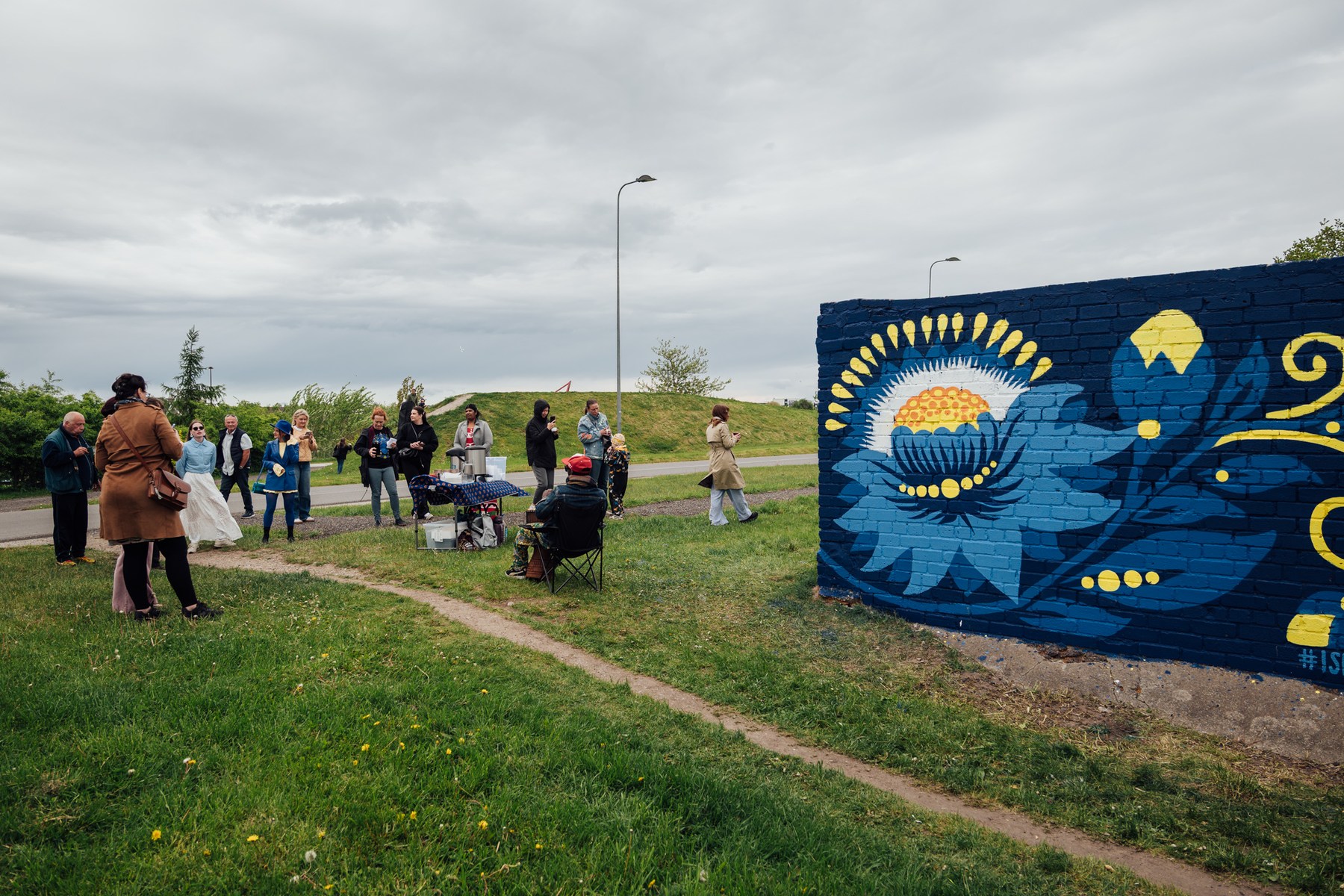Crowd gathering along the grassy path toward the street art piece