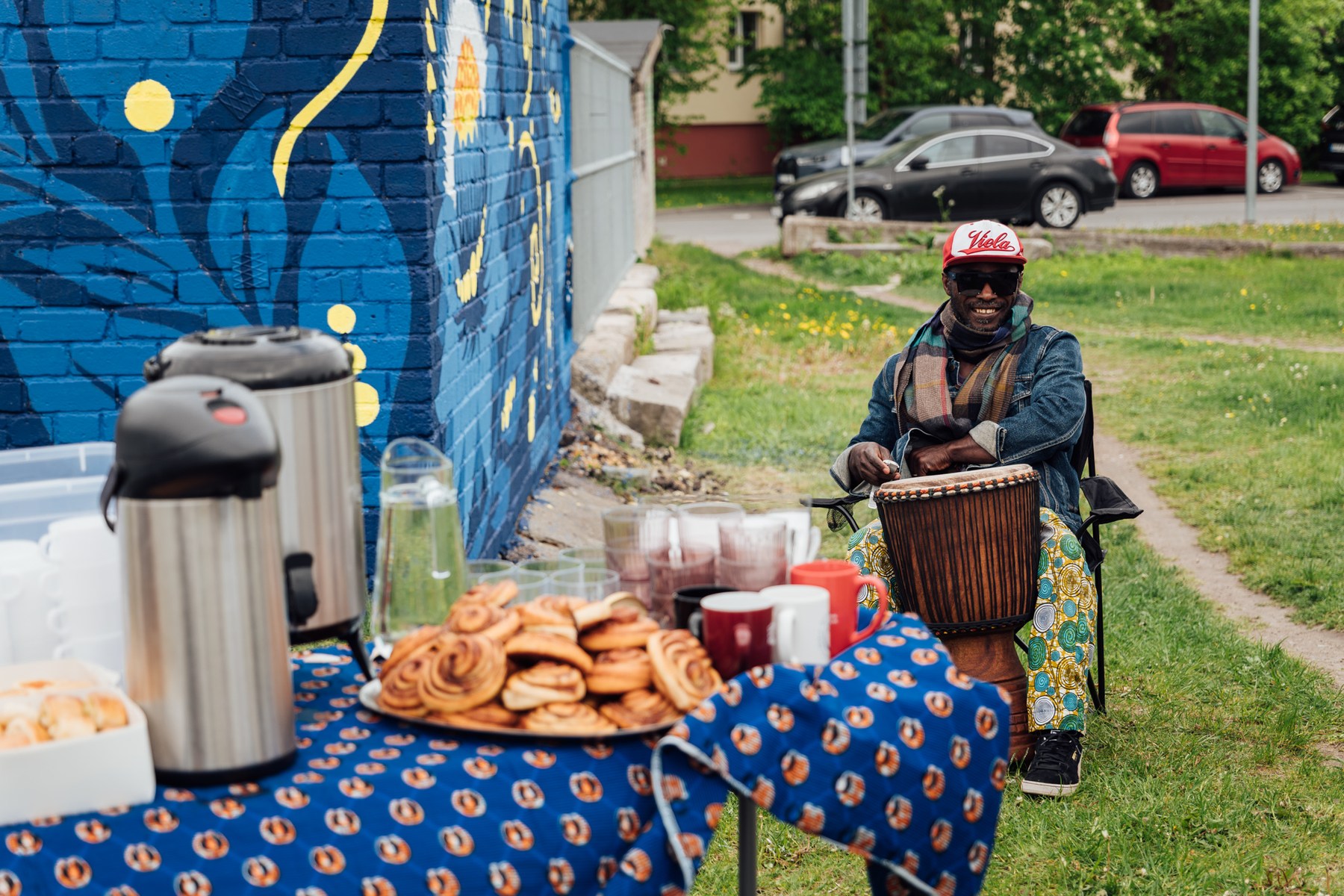 Senam Tsogbe playing djembe before the wall, tea and pastries table in the foreground